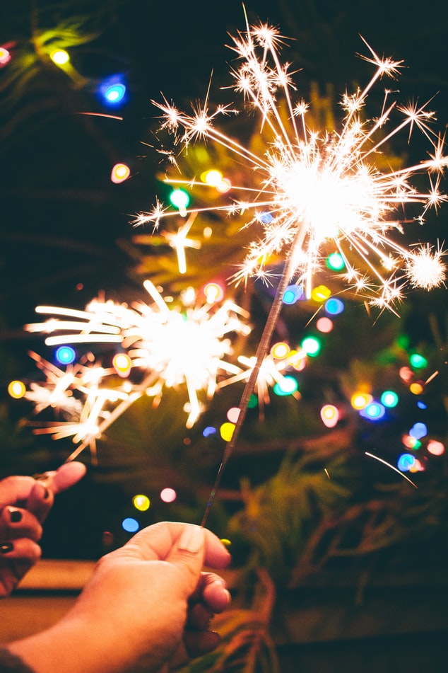 A picture of two lit sparklers being help in front of holiday lights